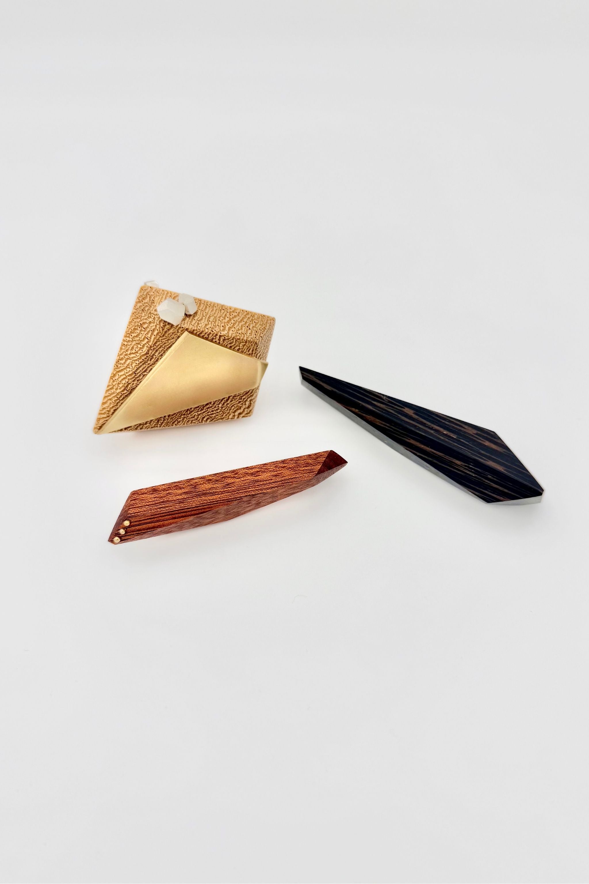 Image of 3 geometric wood brooches, one light blonde in color, one smaller red and a third almost black on a white background