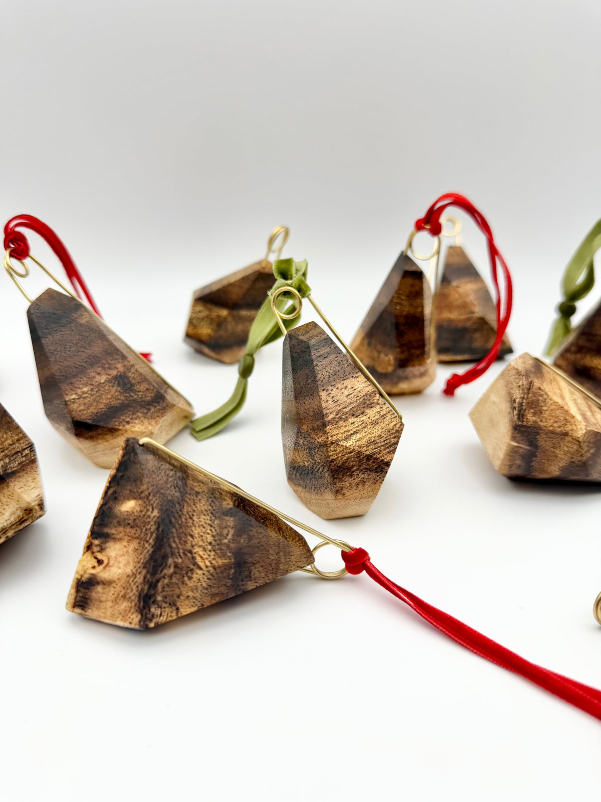 Wooden geometric ornaments with brass details and red and green strings on a white background