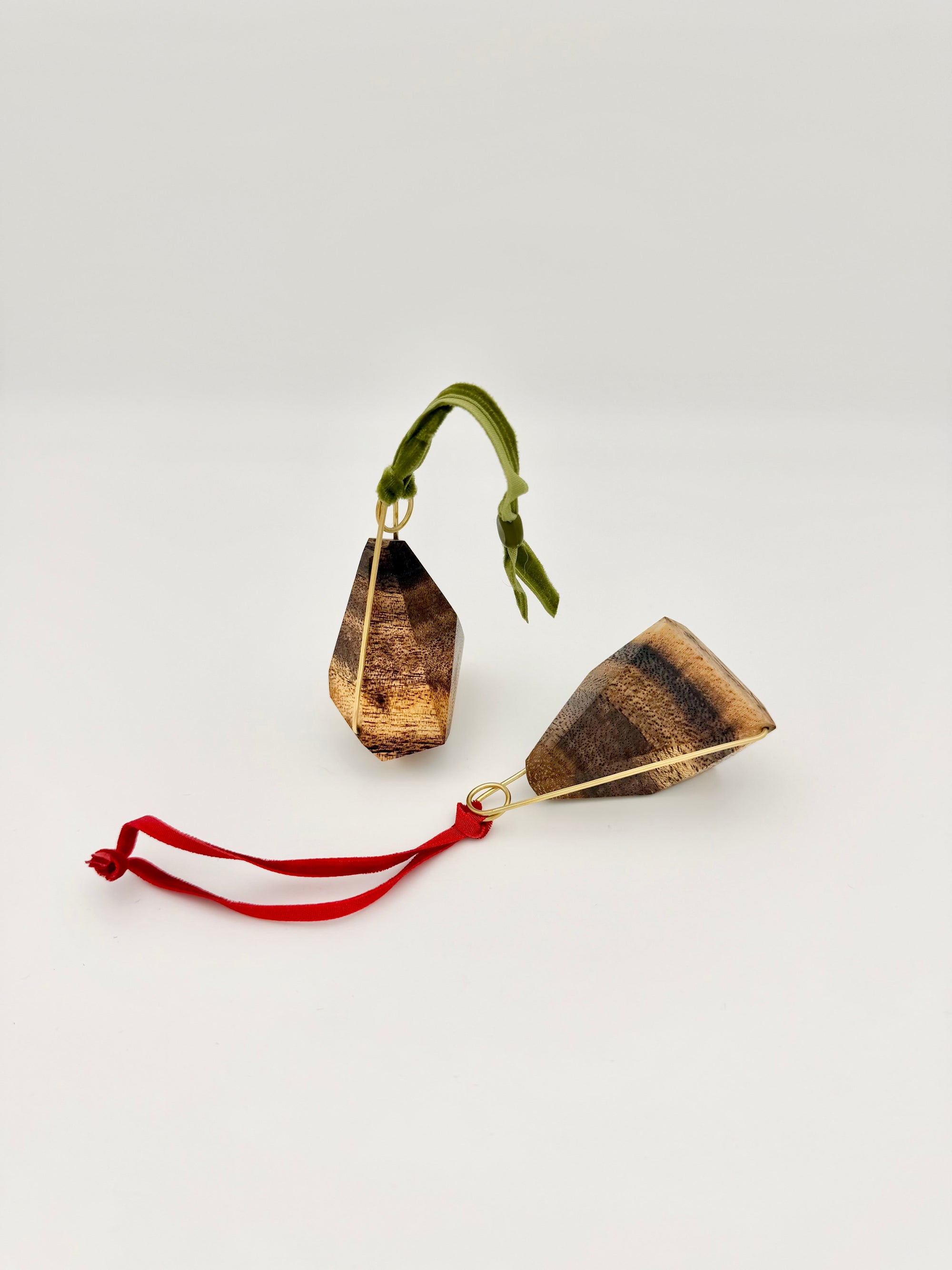 Wood ornaments resembling cones with brass accents and green and red ribbons on a white background