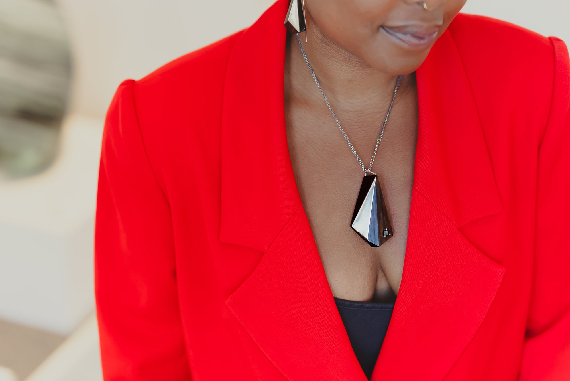 Person wearing a bright red blazer with a blurred background wearing geometric blackwood and silver pendant with a hematite stone. 