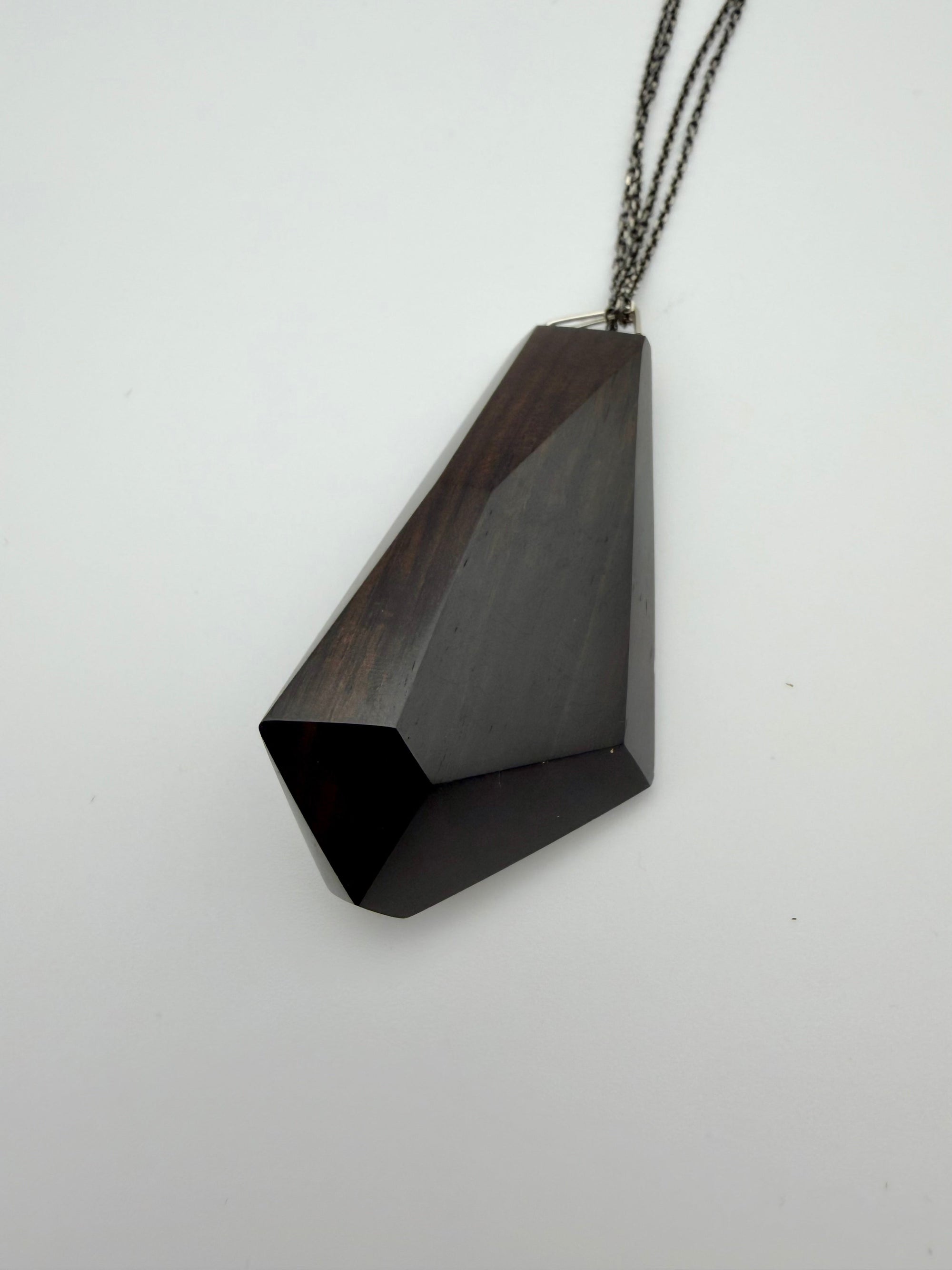 Black geometric pendant on a chain against a white background