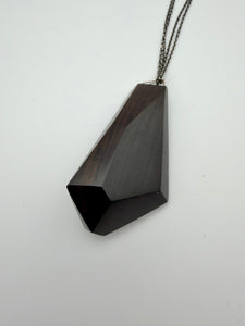Black geometric pendant on a chain against a white background
