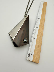Geometric pendant necklace next to a ruler on a light gray background