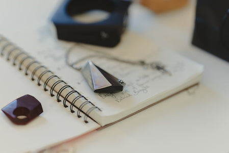 Image of geometric ring and pendant on sketch book with notes and blurry bangle in the background. 