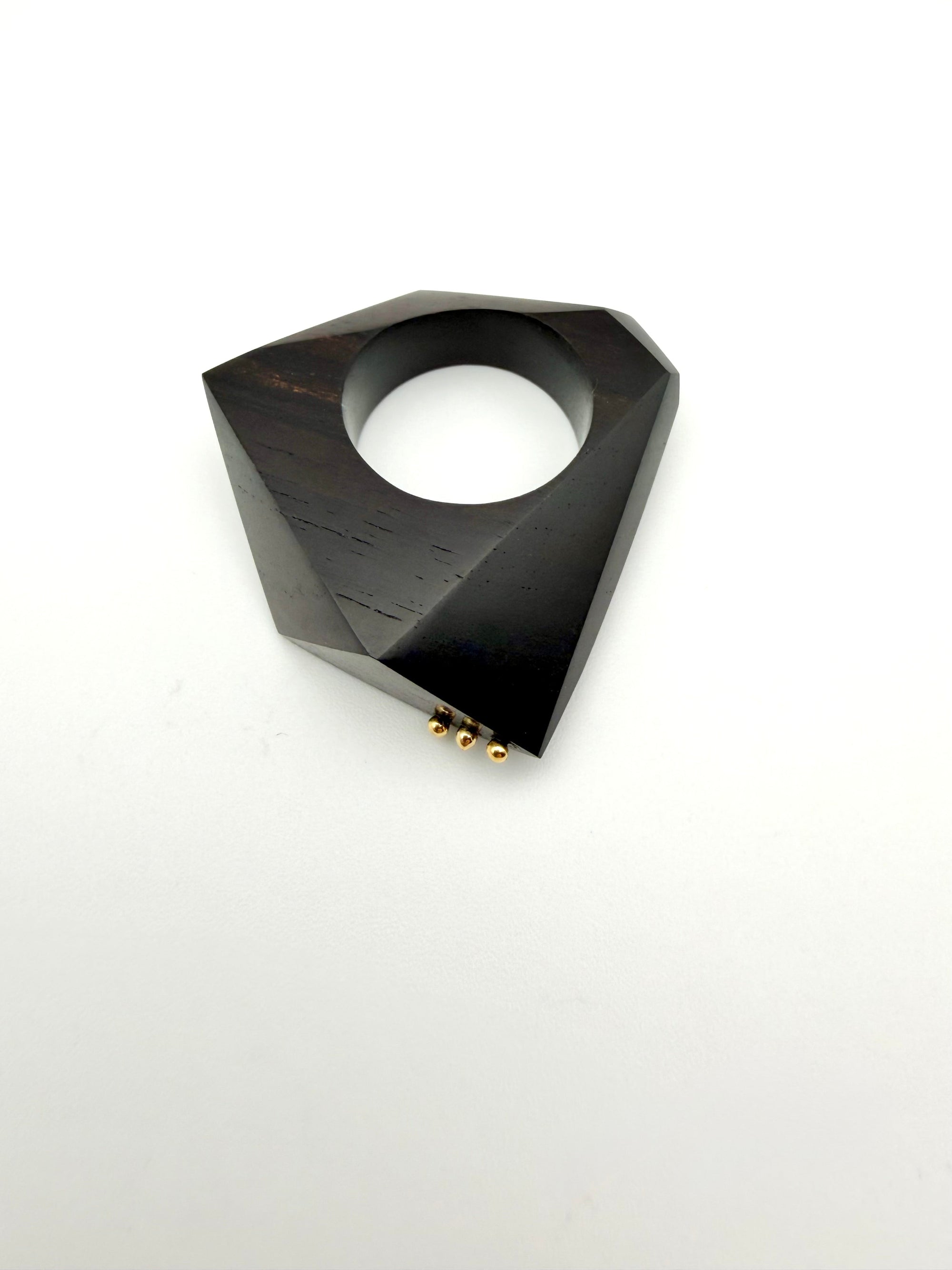 Black geometric ring on its side with gold details on a white background