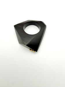 Black geometric ring on its side with gold details on a white background