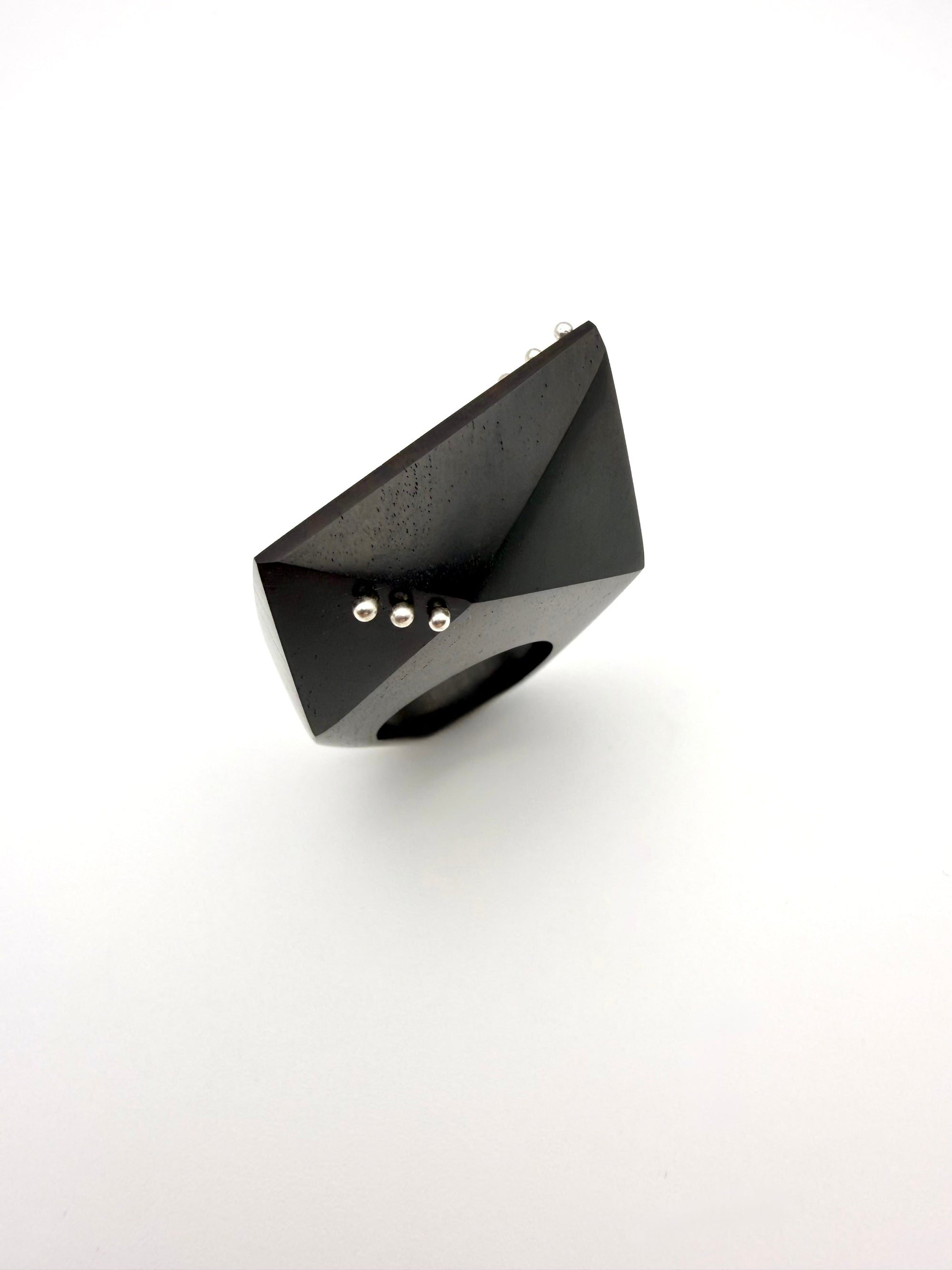 Black geometric jewelry piece with silver details on a white background