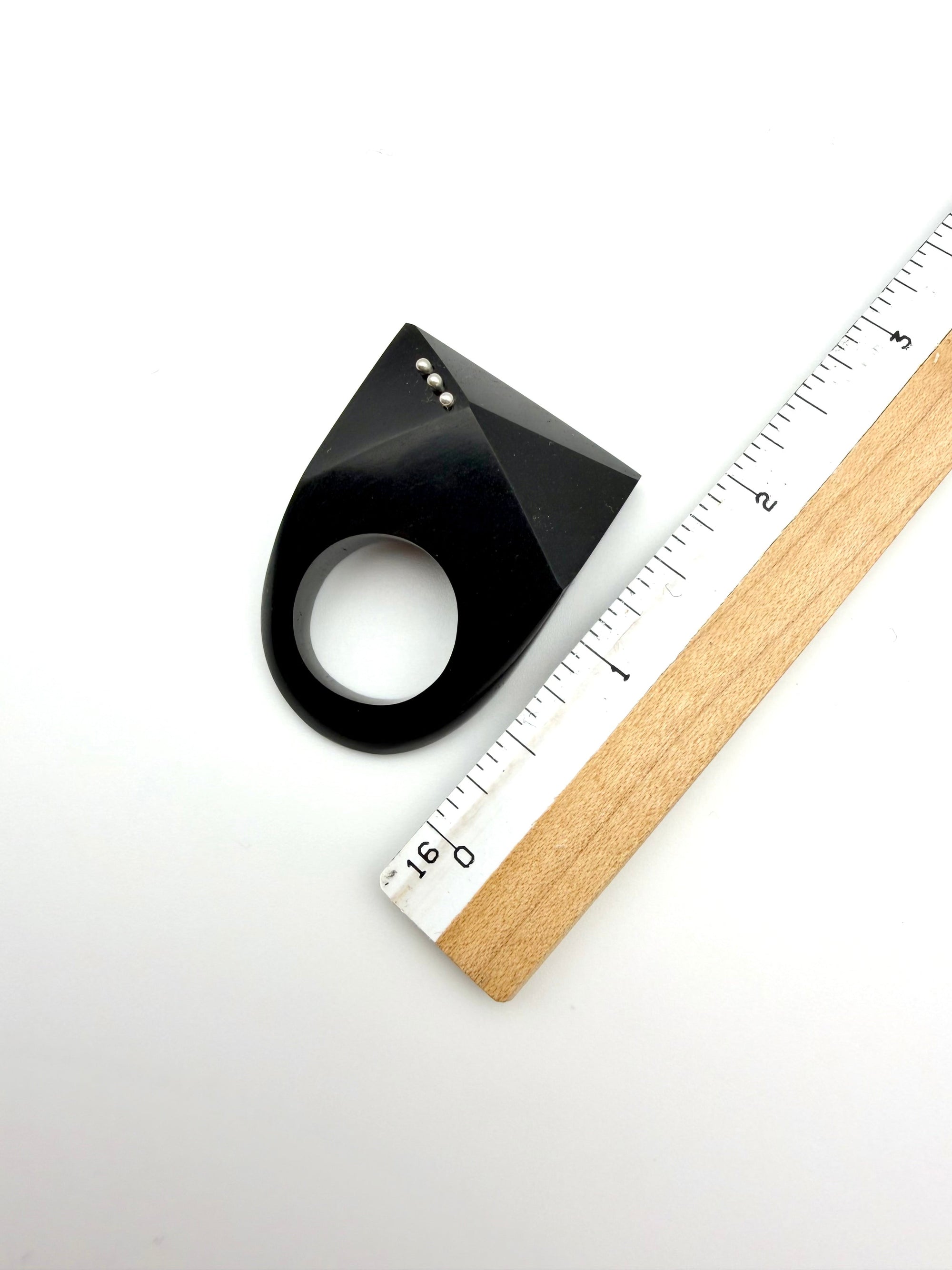 Black and silver ring next to ruler for scale on a white background