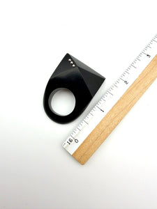 Black and silver ring next to ruler for scale on a white background