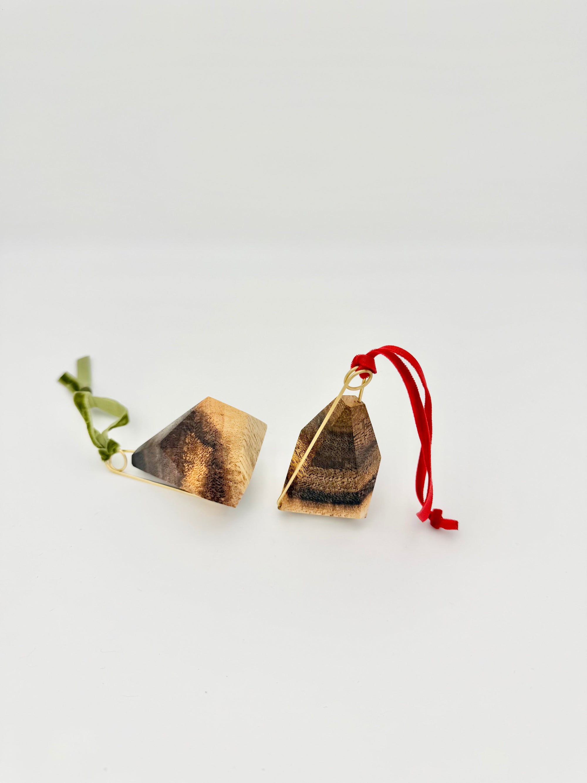 Pair of wood geometric ornaments with brass details and red and green ribbons on a white background
