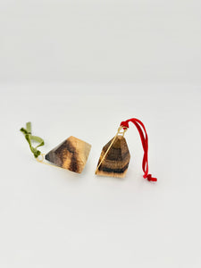 Pair of wood geometric ornaments with brass details and red and green ribbons on a white background