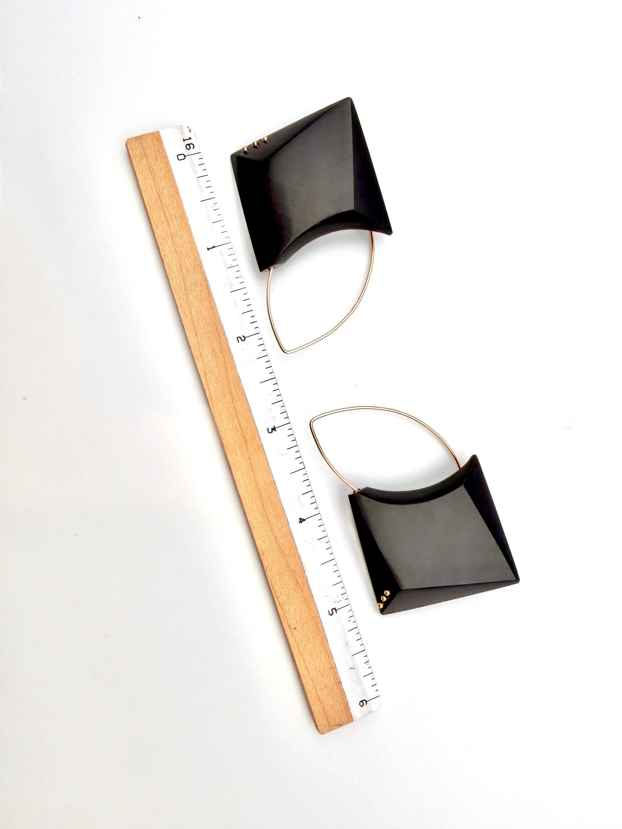 Black square pendant with a wooden ruler for scale on a white background