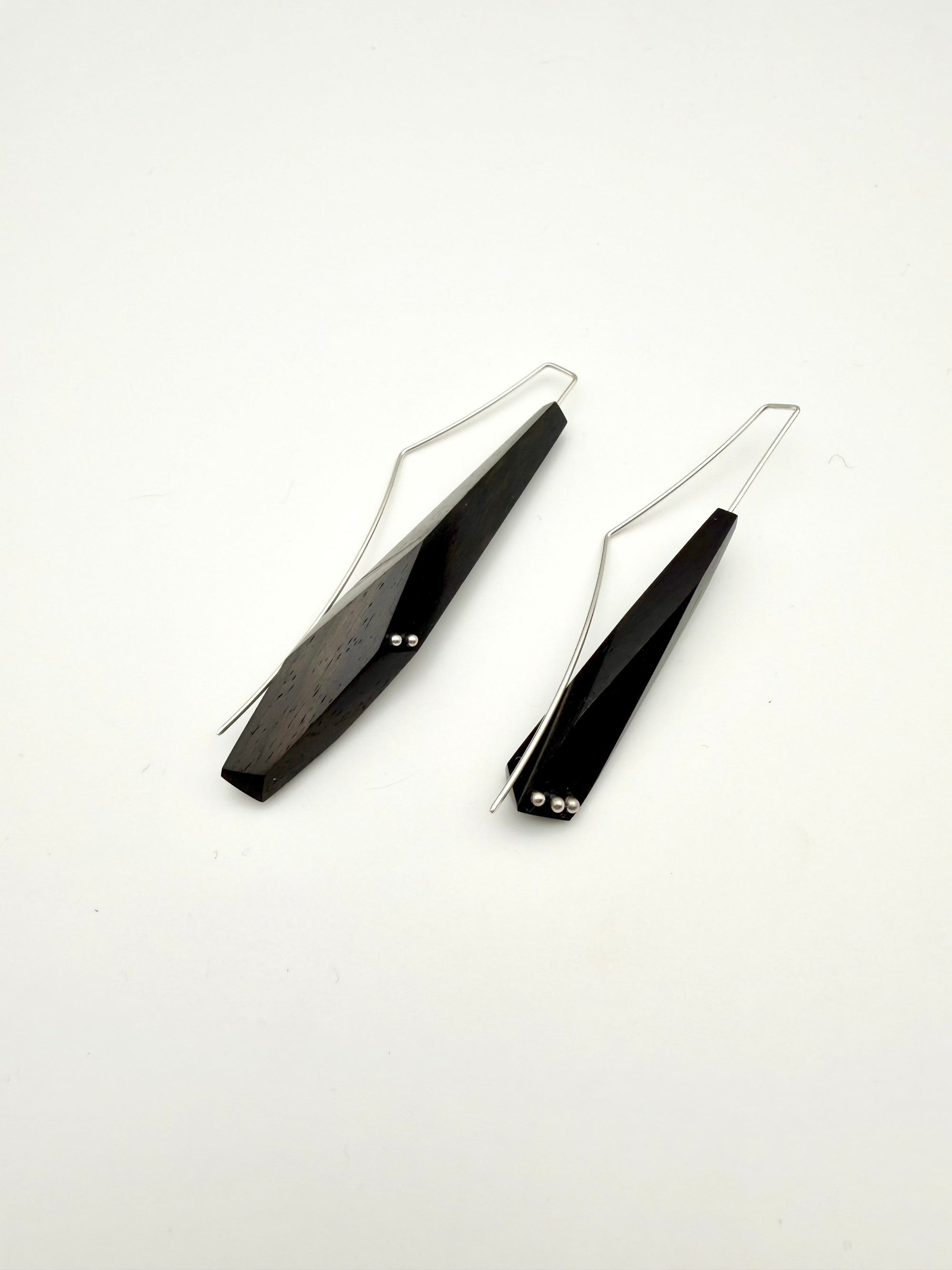 Long black asymmetric geometric pair of wood earrings with silver ear wires and dot details on a white background.