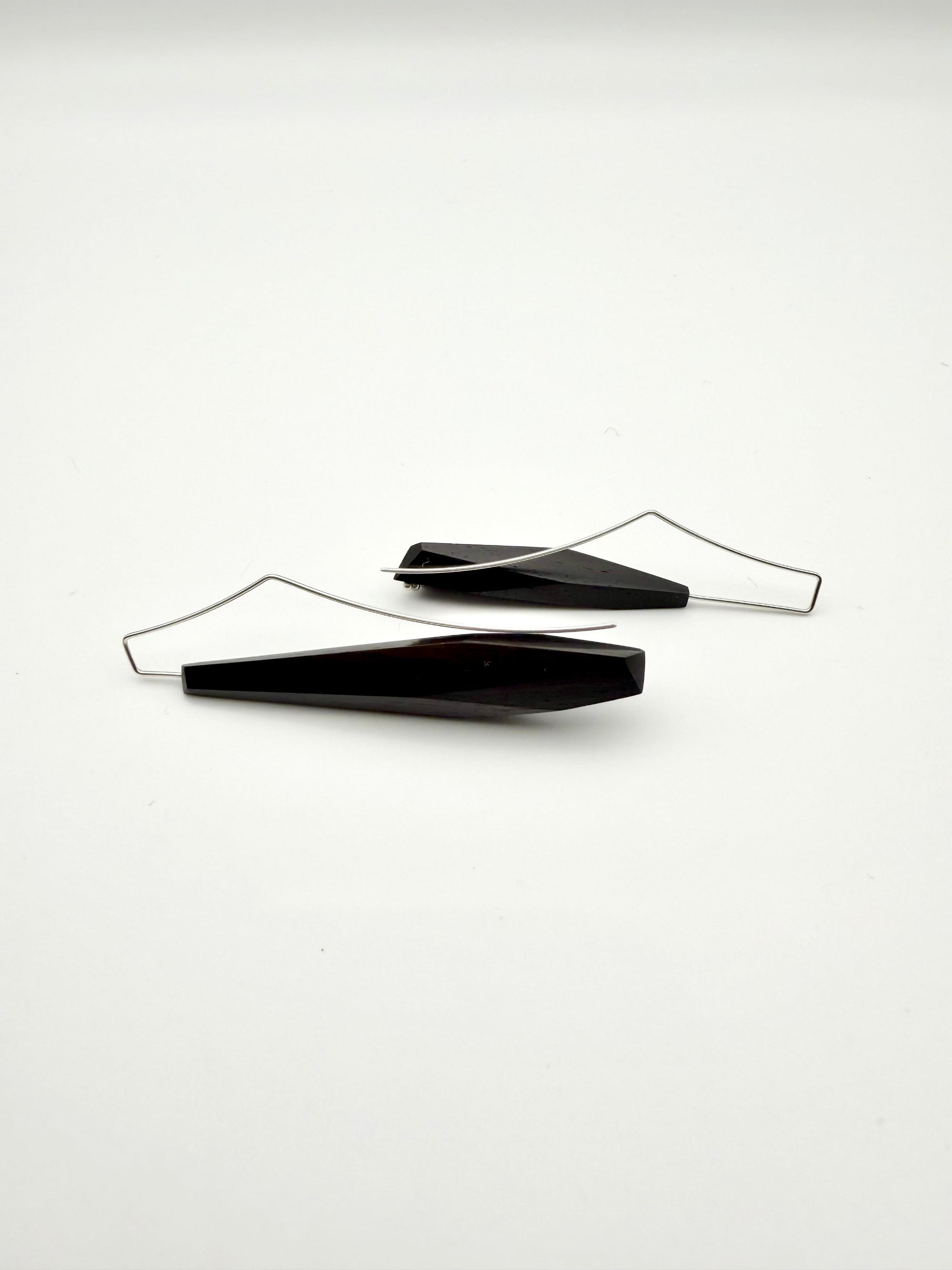 Side view of long black asymmetric geometric wood earrings with silver ear wires and dot details on a white background.