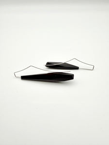 Side view of long black asymmetric geometric wood earrings with silver ear wires and dot details on a white background.