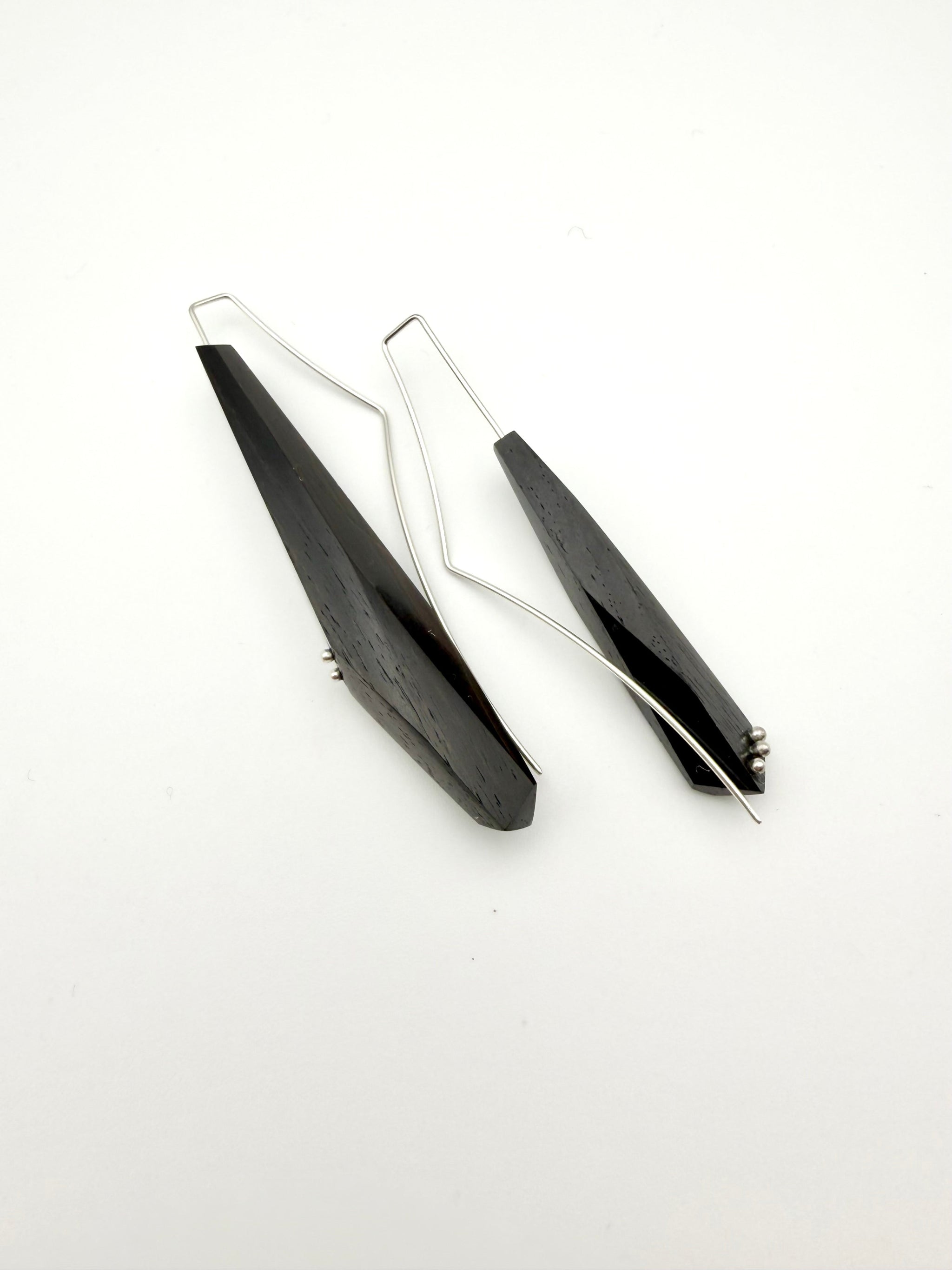Side view of Long black asymmetric geometric pair of wood earrings with silver ear wires and dot details on a white background.