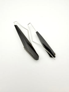 Side view of Long black asymmetric geometric pair of wood earrings with silver ear wires and dot details on a white background.