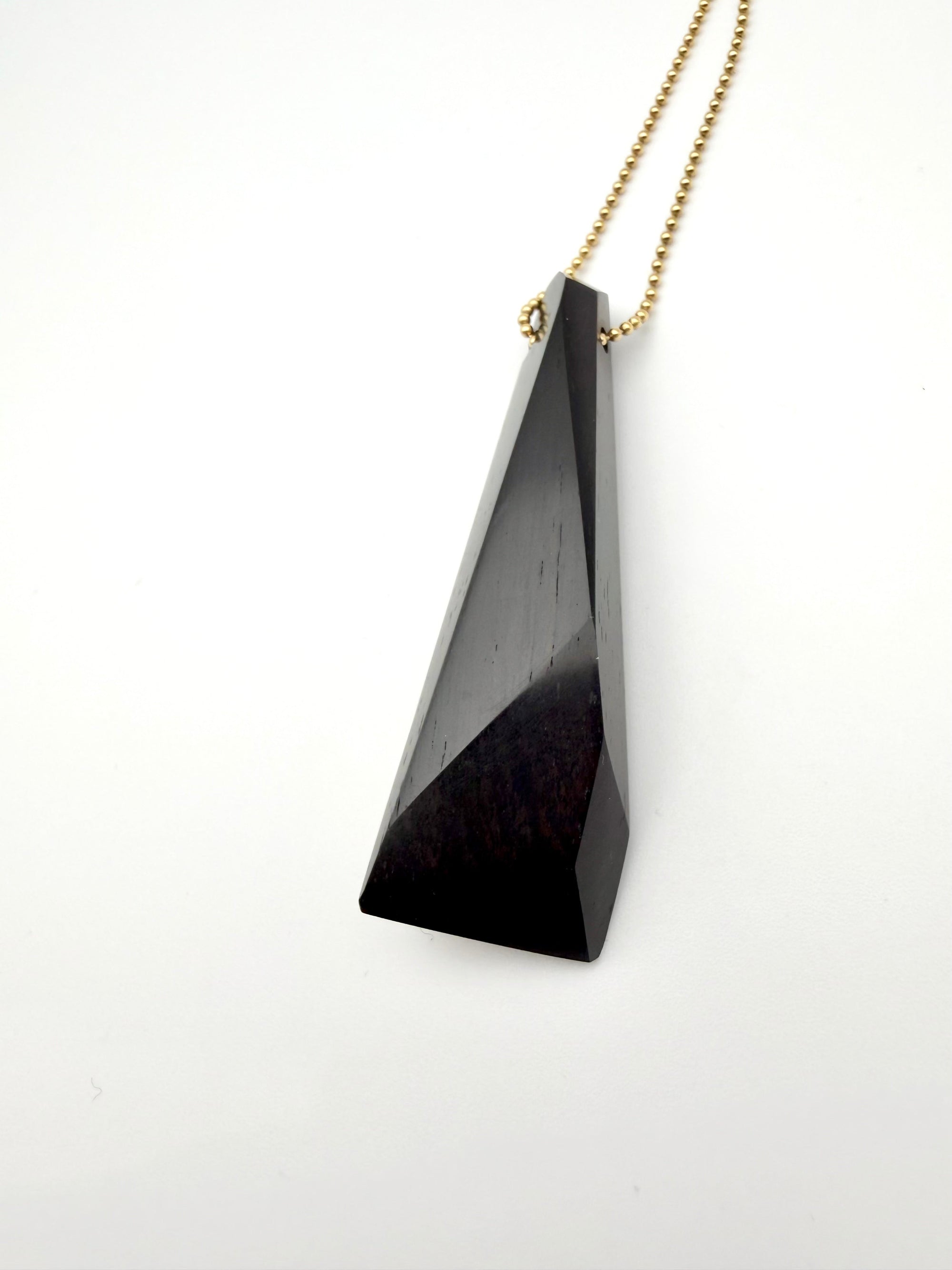 Black triangular pendant on a gold chain against a white background