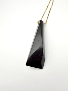 Black triangular pendant on a gold chain against a white background