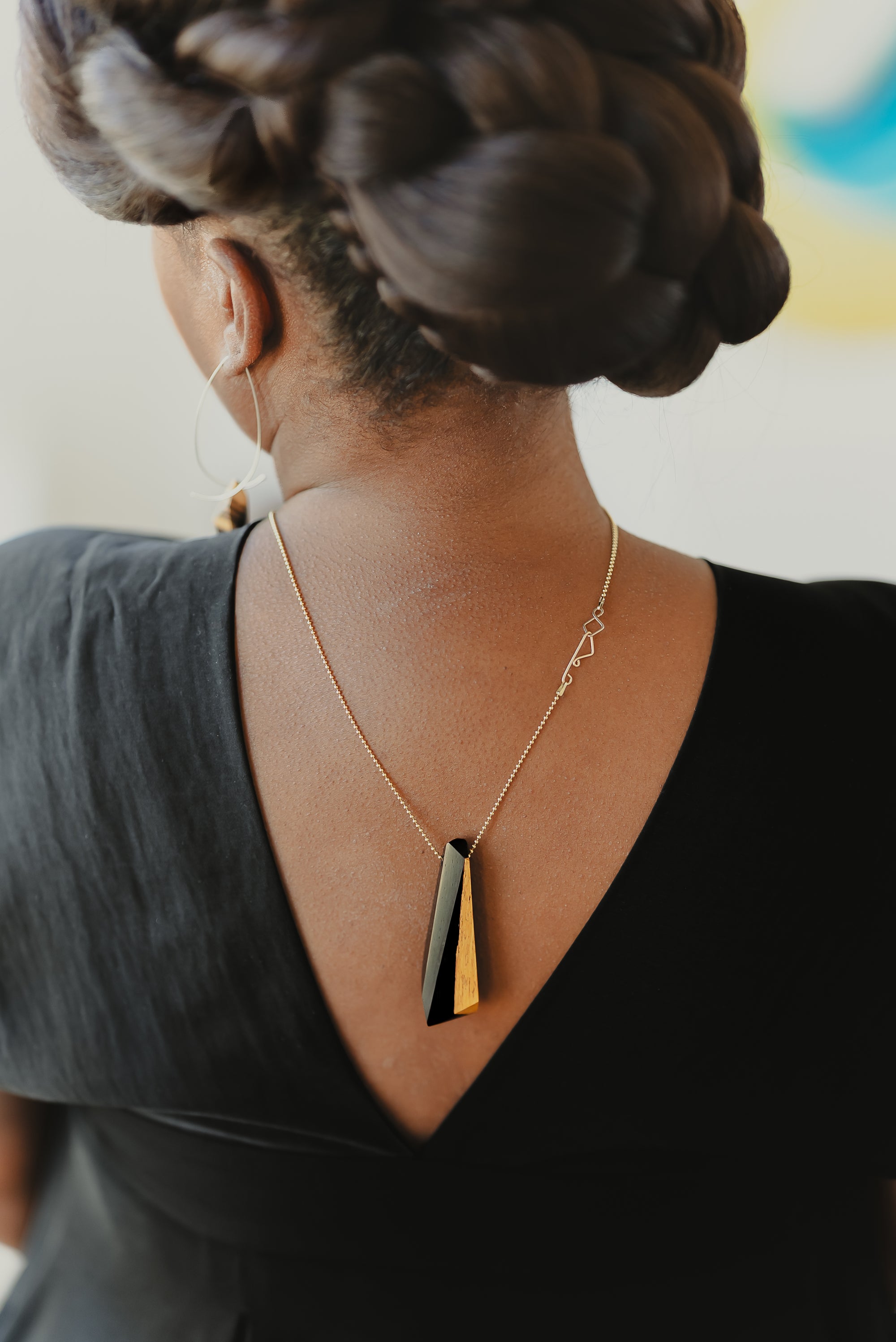 Image of black model wearing a black wood necklace with a gold chain hanging on her back. 