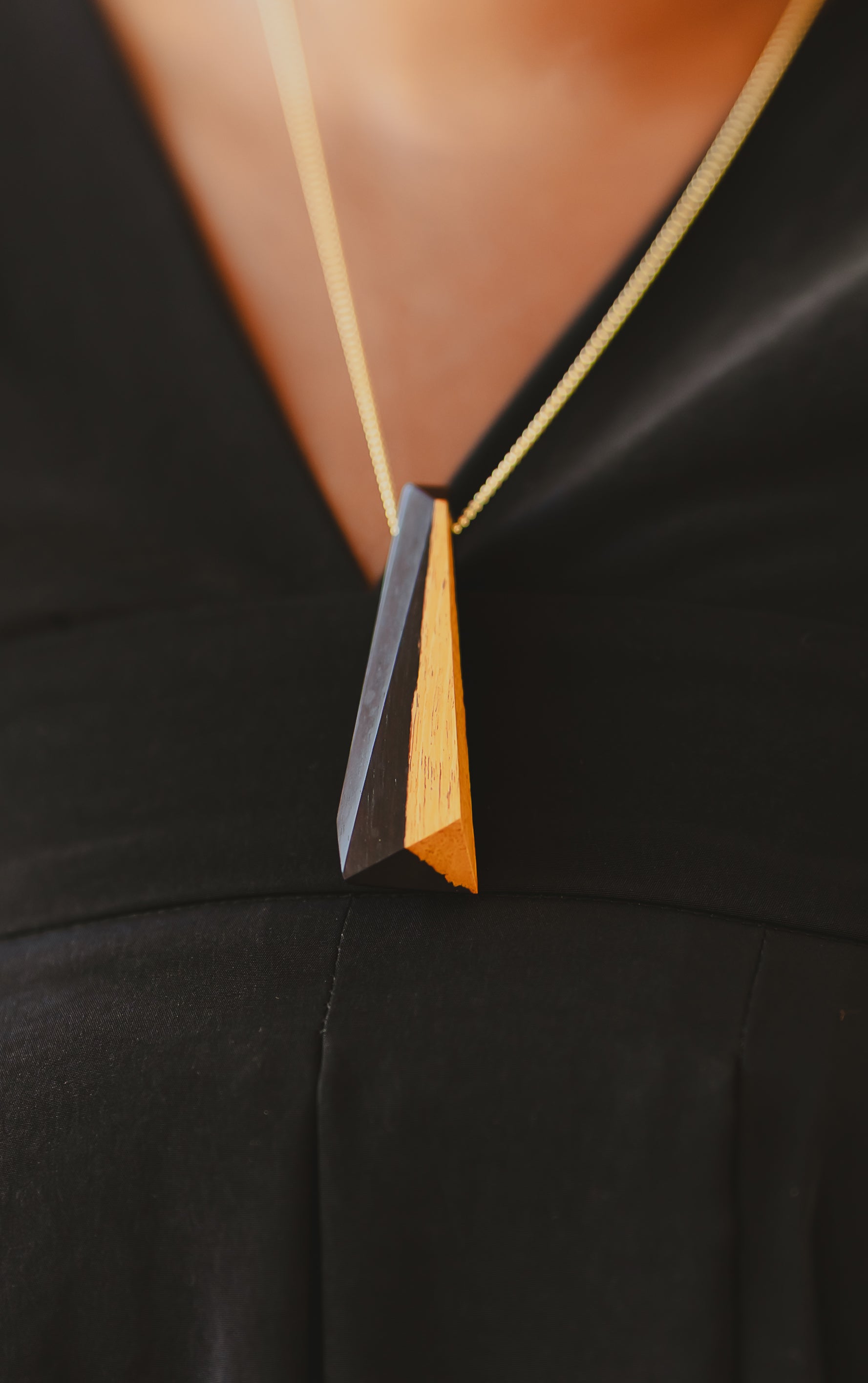 Black and gold tone wood pendant on model close up with black v neck dress on gold chain. 