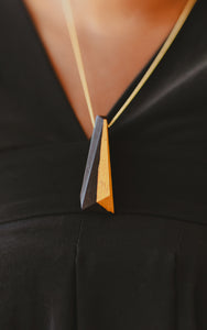 Black and gold tone wood pendant on model close up with black v neck dress on gold chain. 