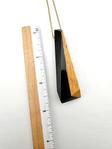 Black and tan wood pendant hanging next to a ruler on a white background