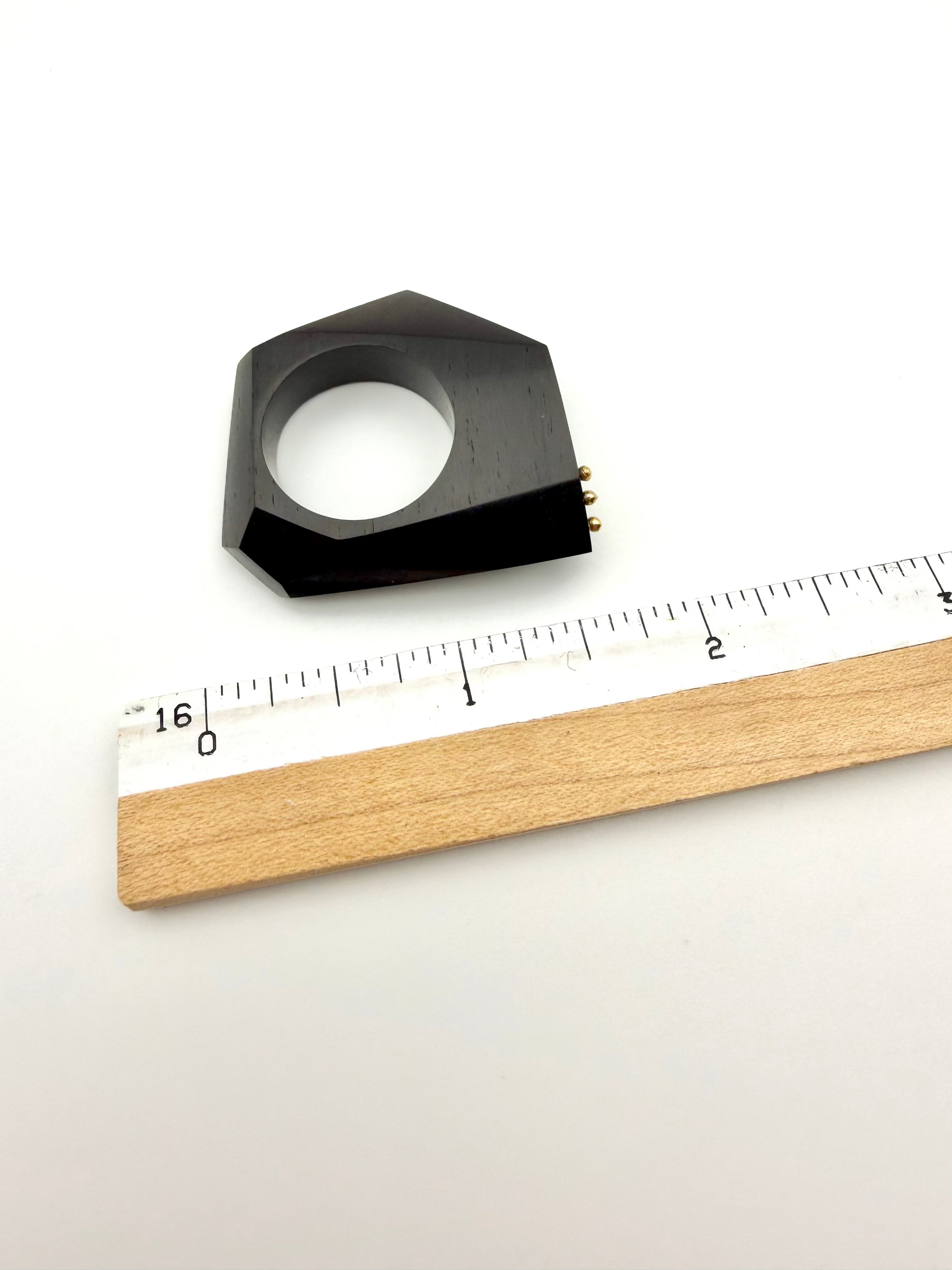 Black wood sculpture ring next to a ruler on a white background