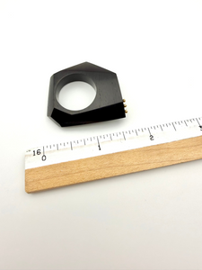 Black wood sculpture ring next to a ruler on a white background
