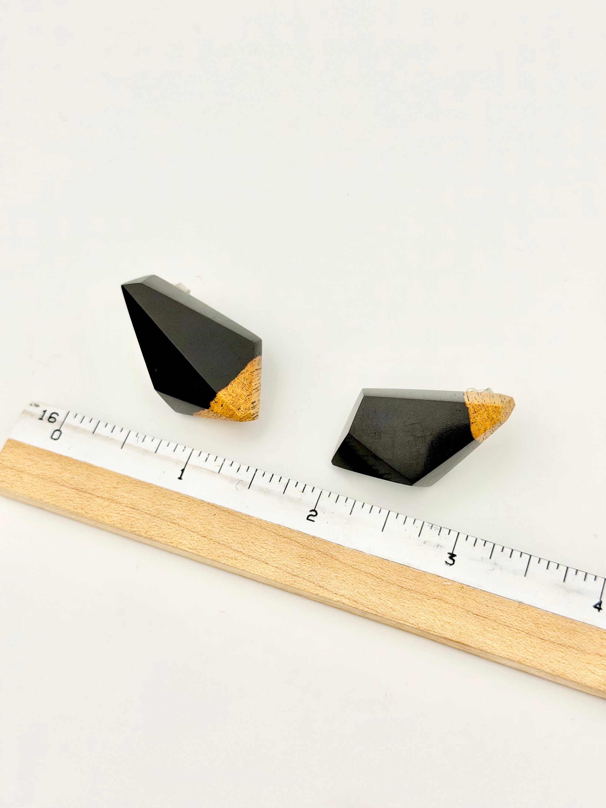 Black wood geometric earrings with gold accents on a white background with a ruler for scale.