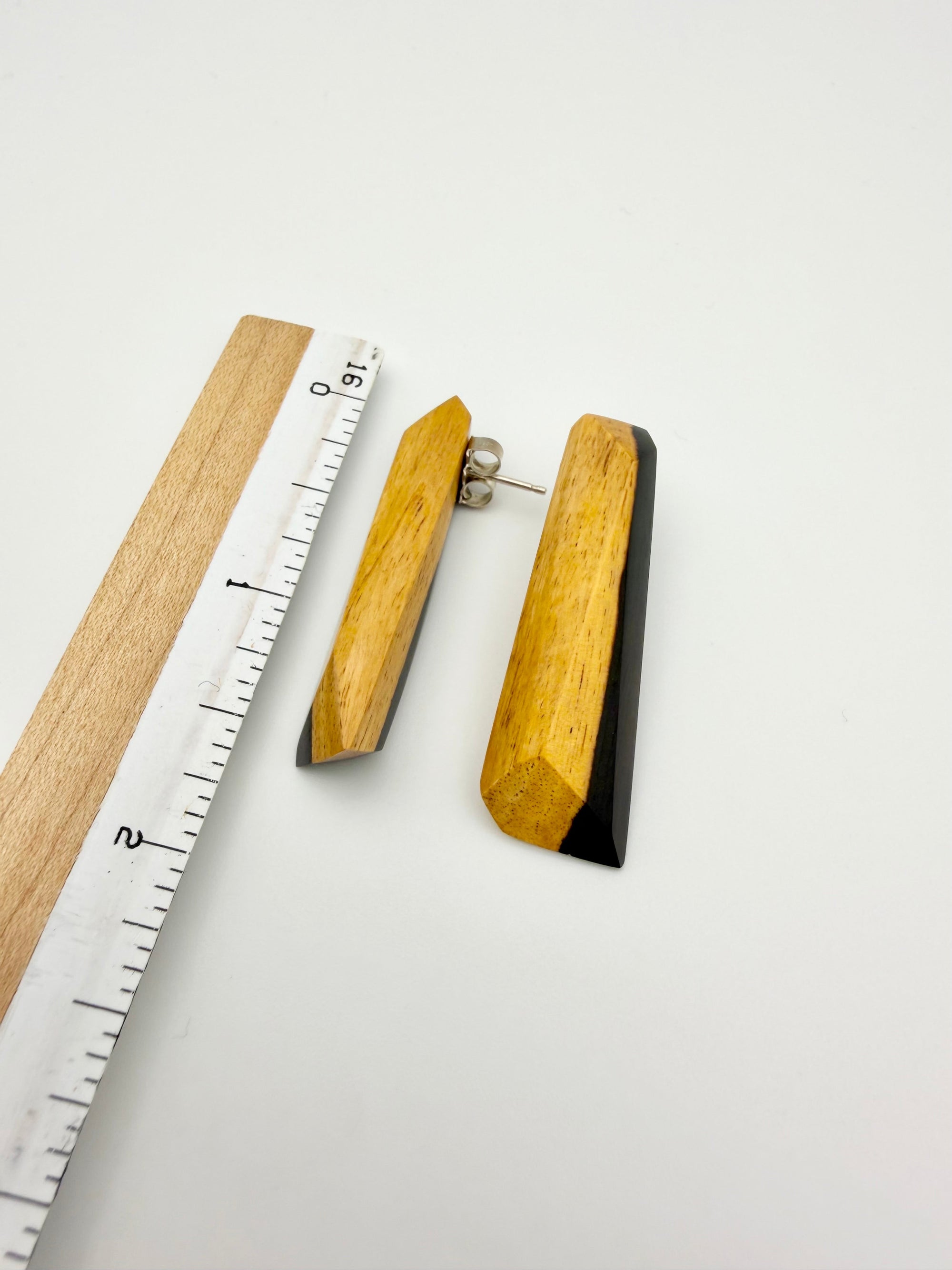 Pair of black and tan long wood stud earrings next to ruler to show scale about 1.5" long