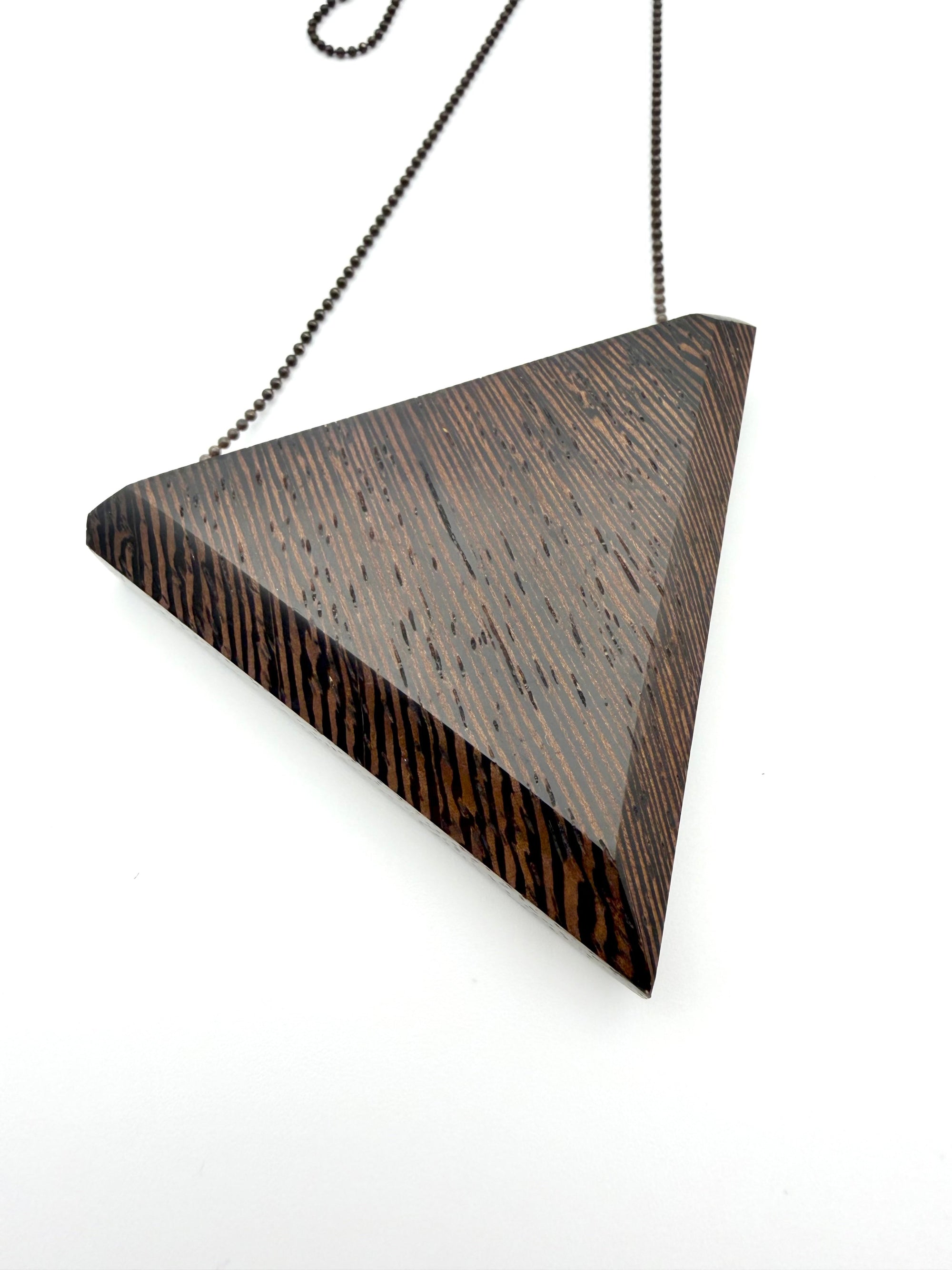 Detail back view of triangular pendant with wavy wood grain pattern on a white background 