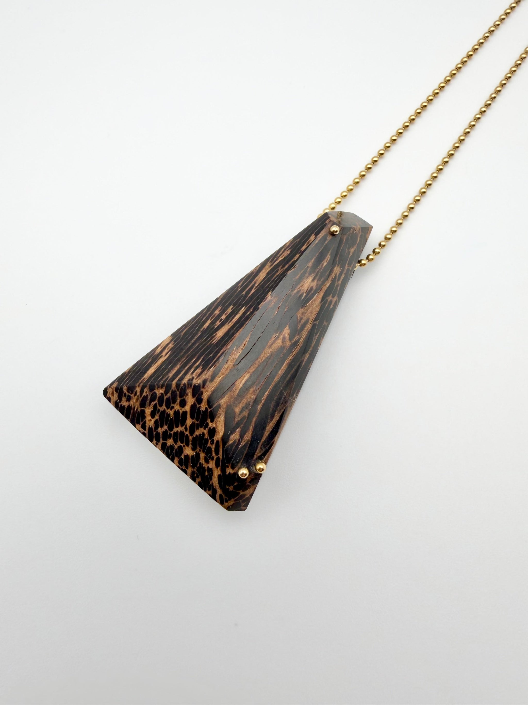 Triangle-shaped pendant with a gold chain on a light gray background