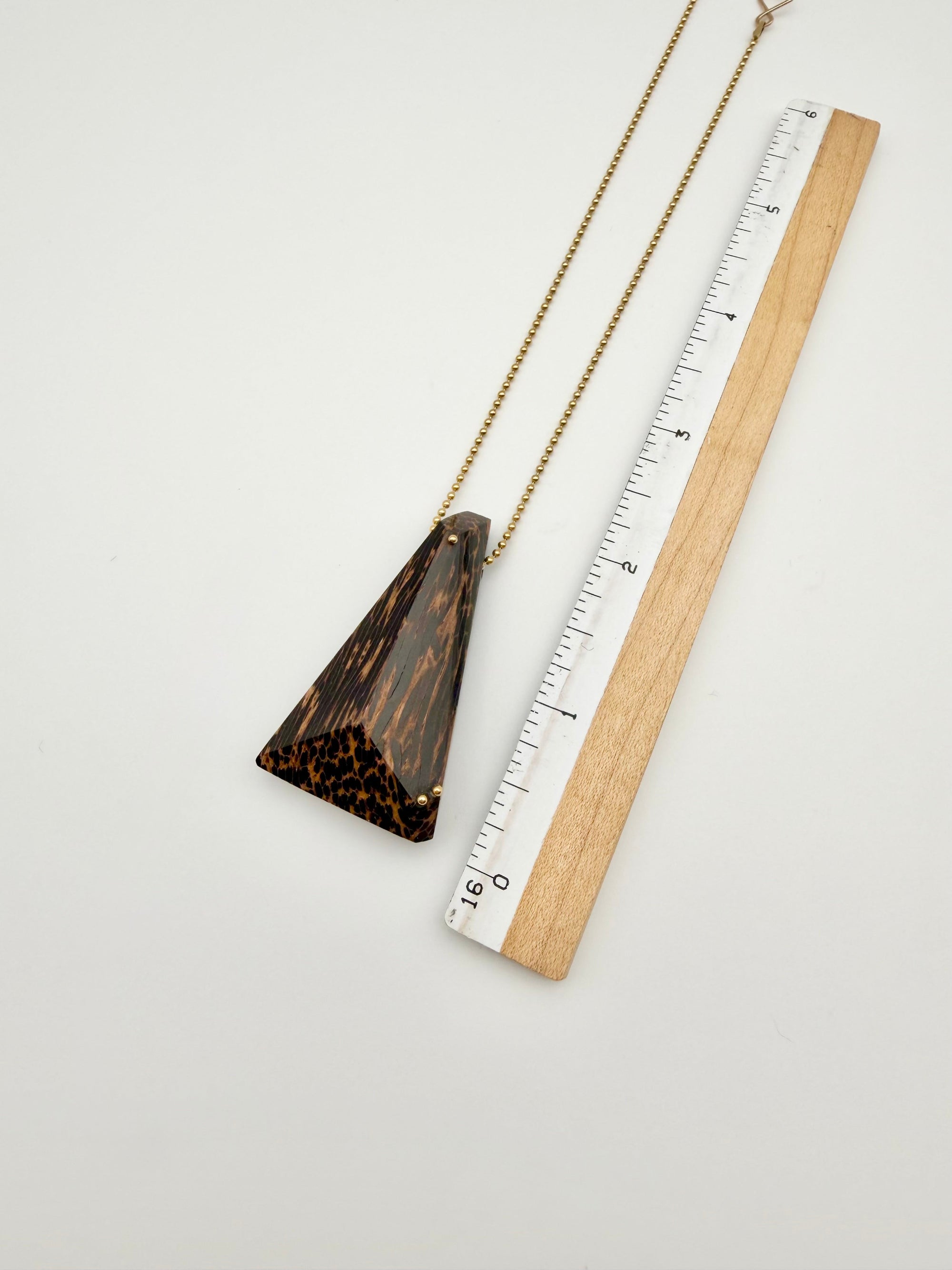 Black Palm wood pendant necklace next to a ruler on a light gray background