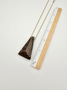 Black Palm wood pendant necklace next to a ruler on a light gray background