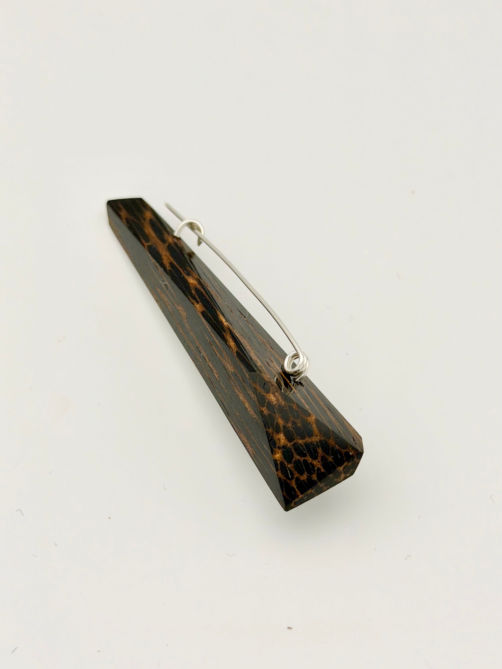 Black and brown geometric wood brooch with silver pin on white background. 