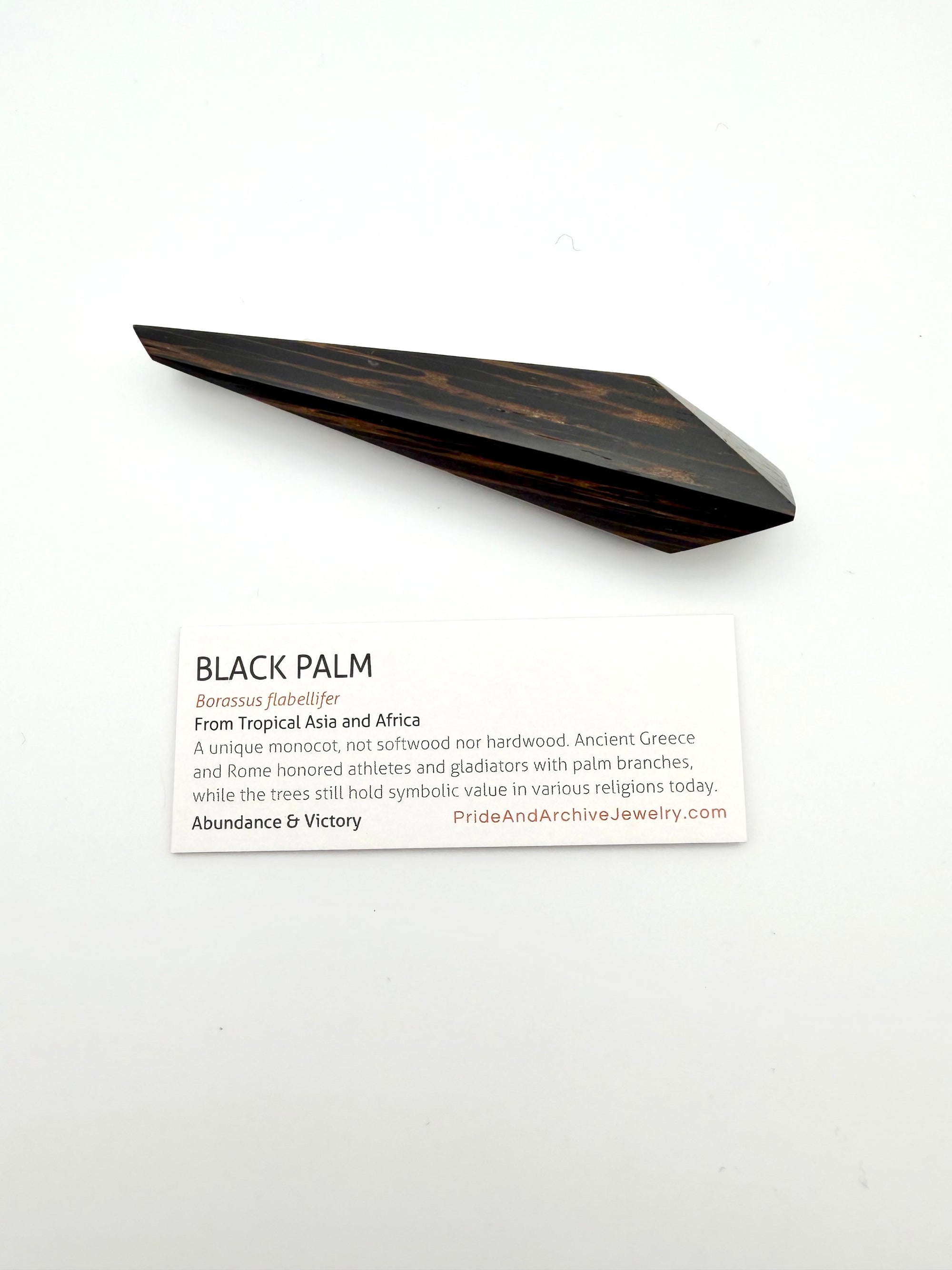 Wooden palm leaf on a white background with informational card sitting below it.