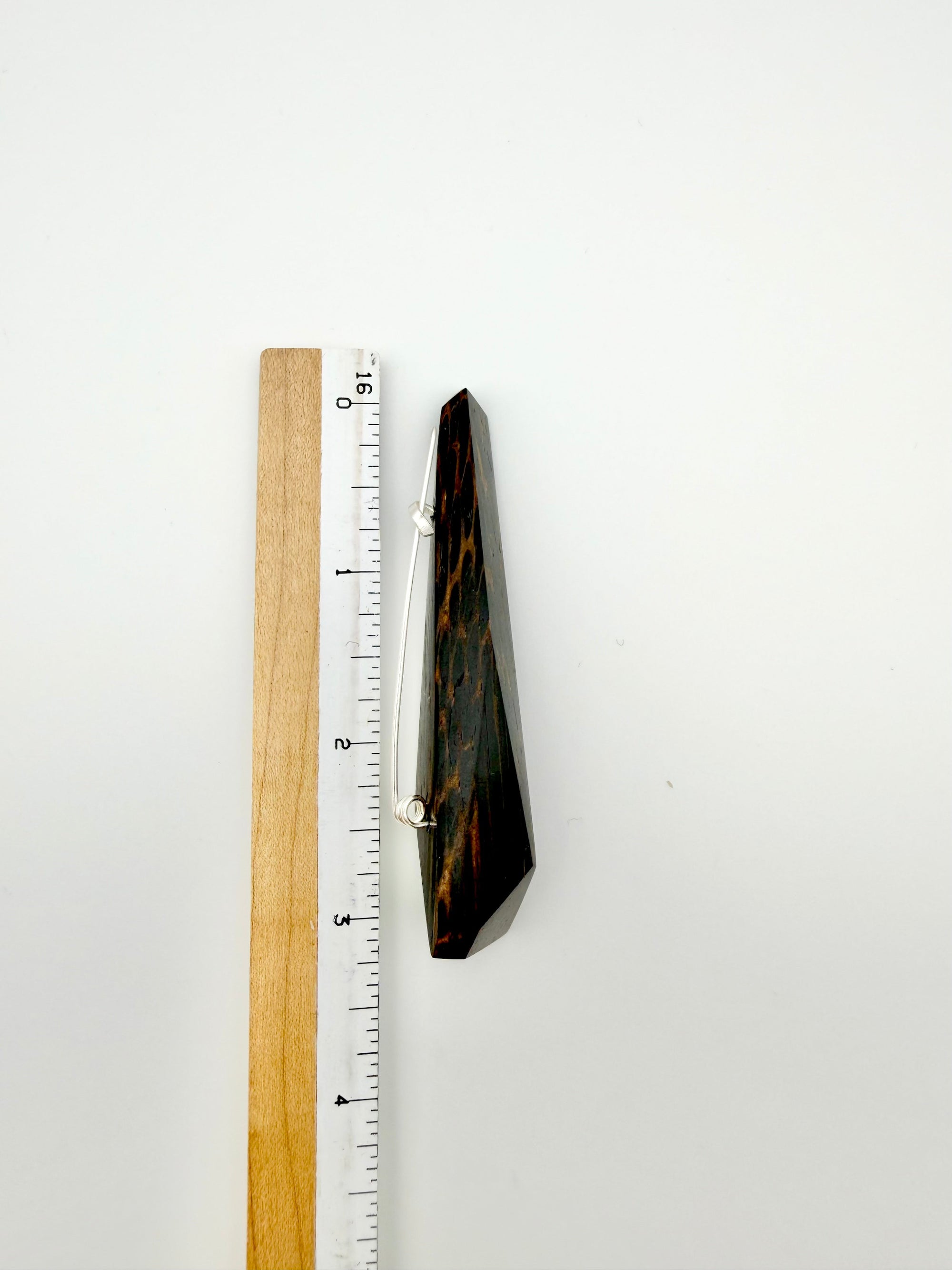 Black and brown geometric wood brooch next to ruler for scale on white background. 