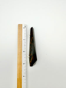 Black and brown geometric wood brooch next to ruler for scale on white background. 