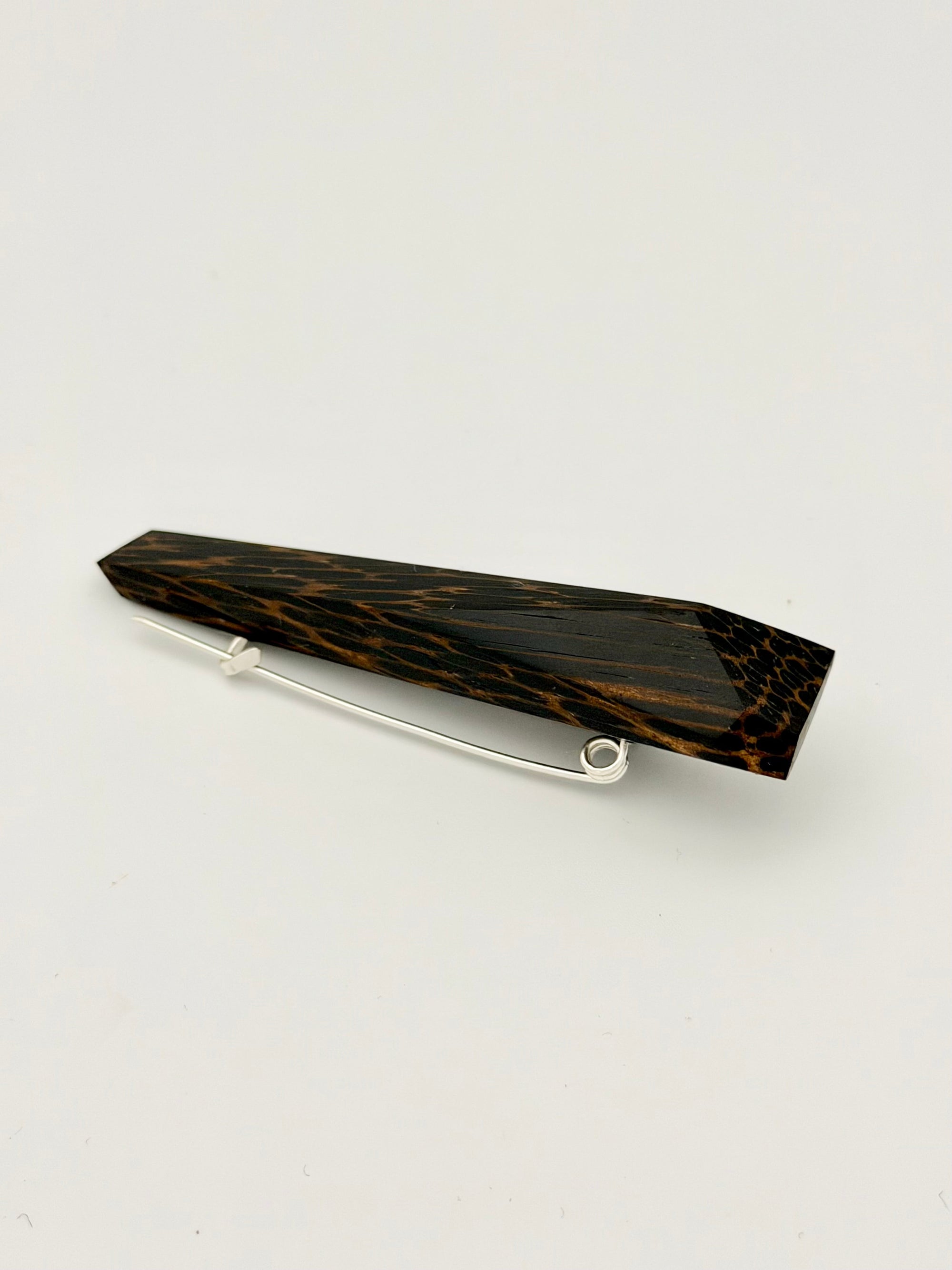 Black and brown geometric wood brooch on white background. 