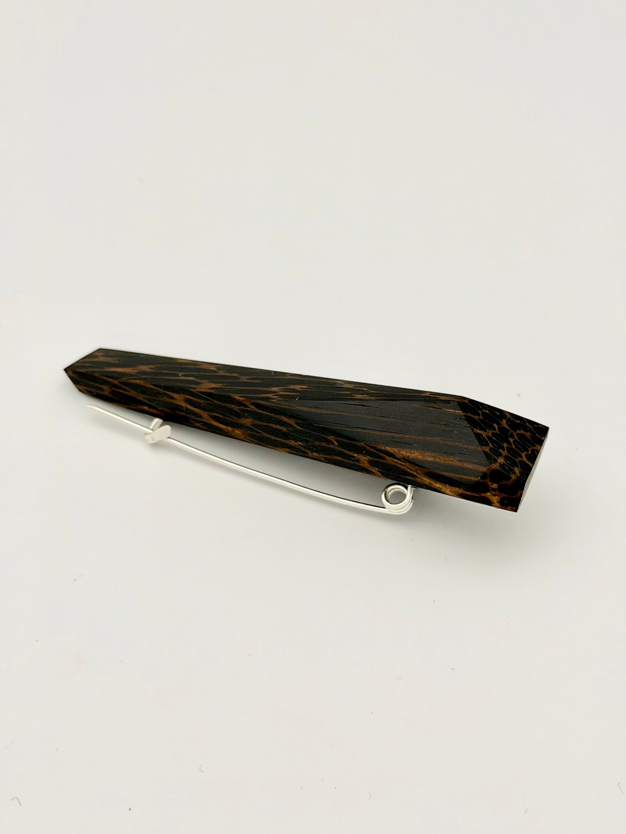 Black and brown geometric wood brooch on white background. 