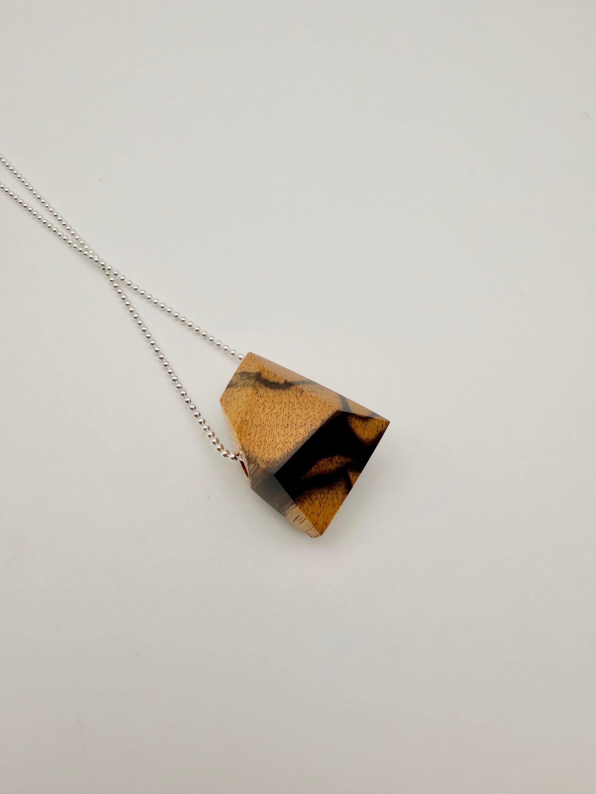 Necklace with a geometric polished Black & White ebony wood pendant (resembling a stone) on a silver bead chain and light background
