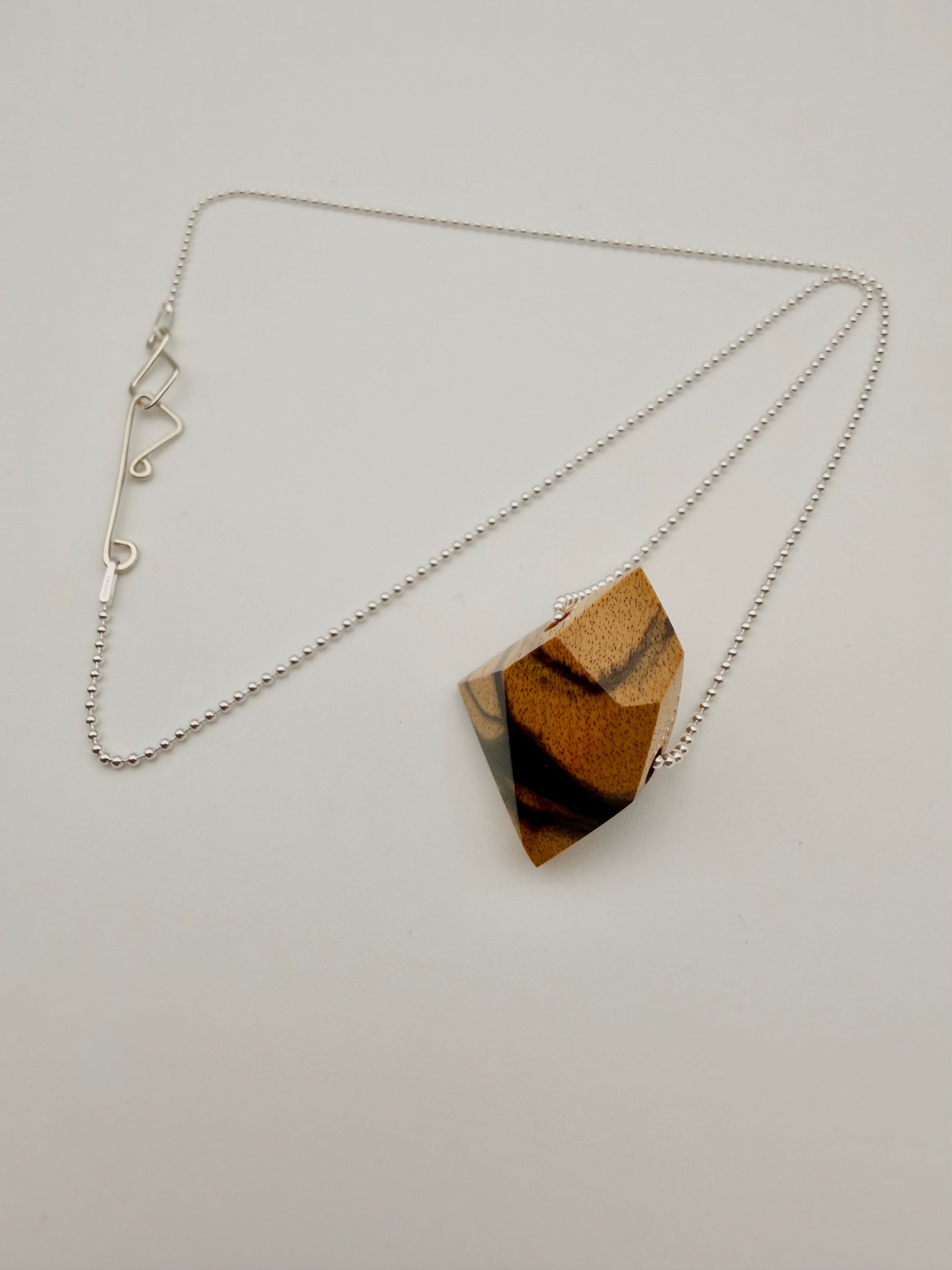 Necklace with a geometric polished Black & White ebony wood pendant (resembling a stone) on a silver bead chain and custom clasp on light background.