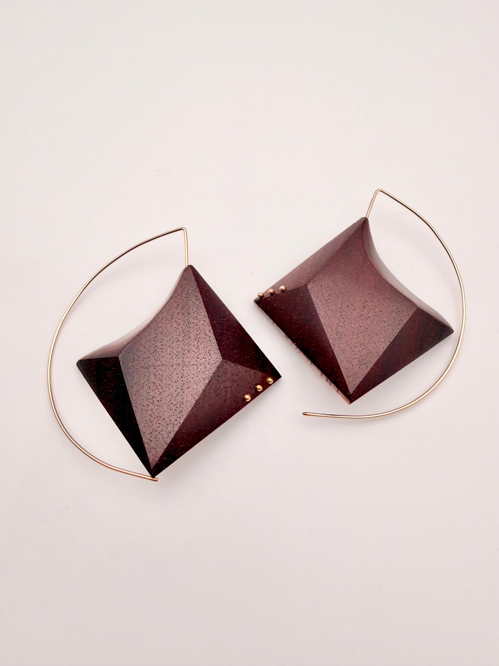 Pair of geometric wood earrings with a gold hoop and burgundy pyramid-shapes on a light background.