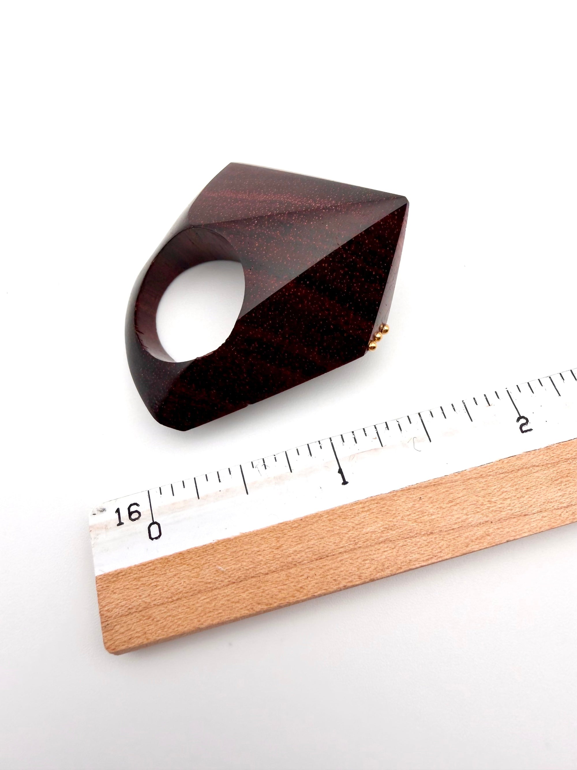 Wooden ring with geometric design next to a ruler on a white background