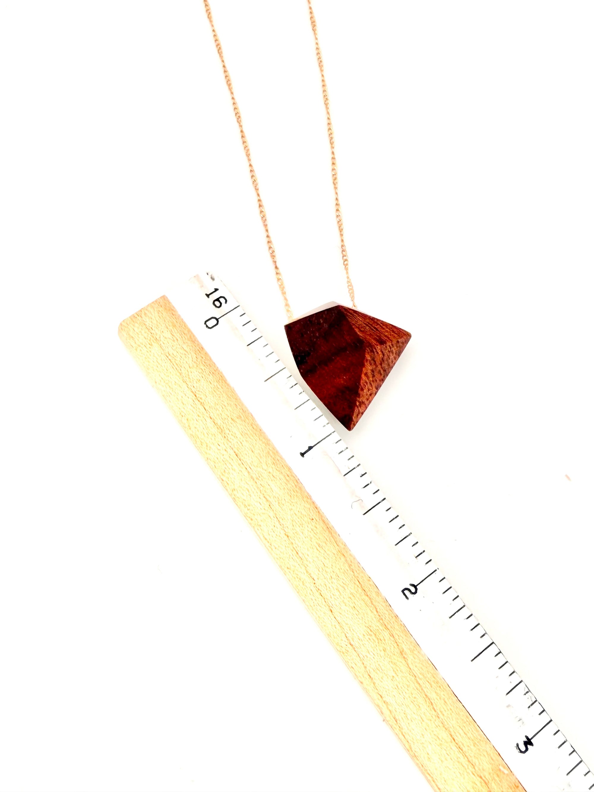 Deep red wood geometric necklace next to a ruler for scale on white background. 