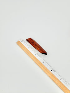 Red geometric wood brooch next to ruler for scale on white background. 