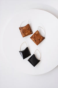 two pairs of wood geometric earrings, one blackwood and the other pair featured above it on a circular display is an orange color with dramatic wood grain set on a white background. 