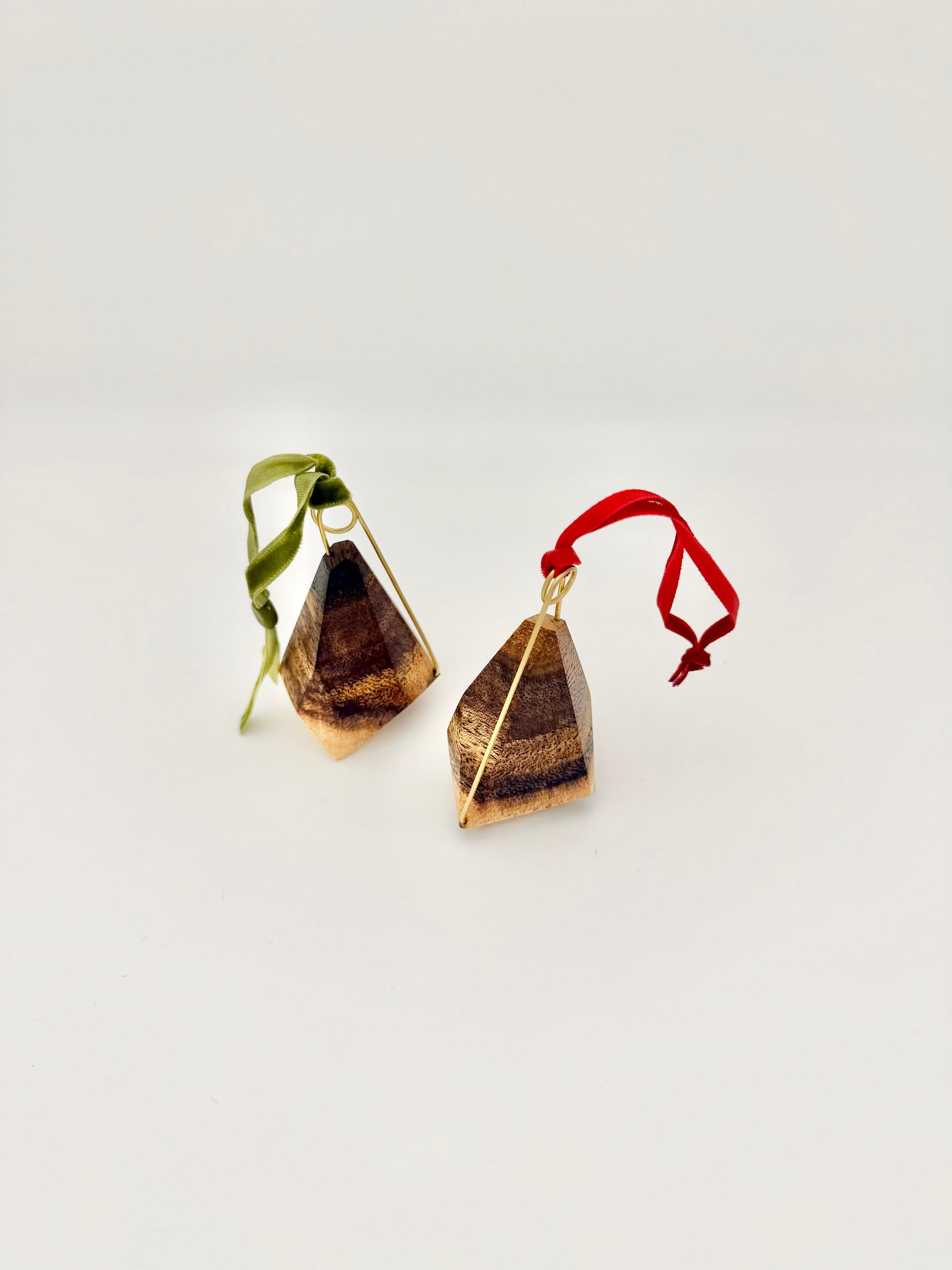 Pair of wood geometric ornaments with brass details and red and green ribbons on a white background