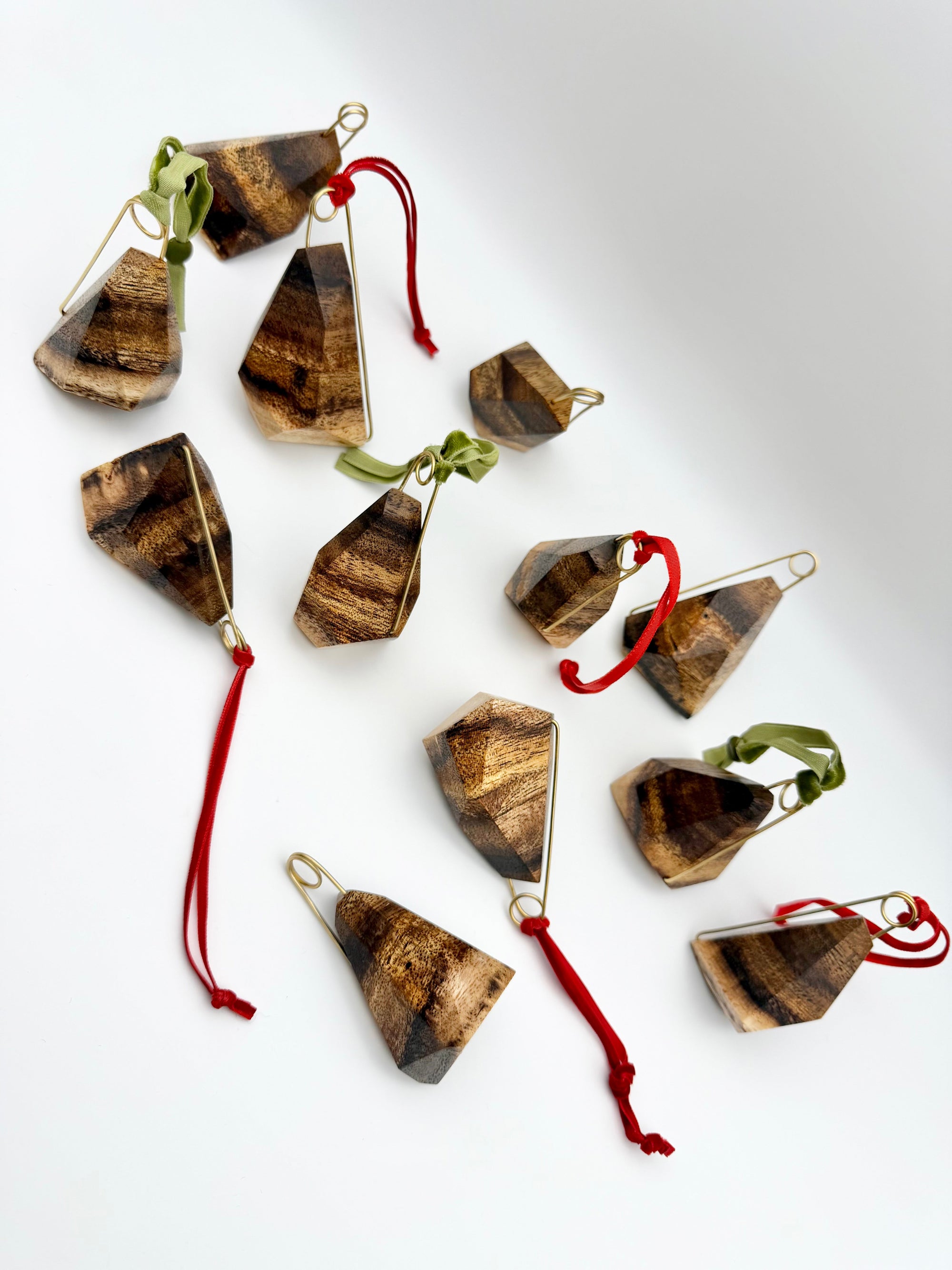 Geometric Wood Ornaments with brass details and red and green ribbons on a white background. 